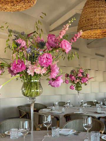 Centros de mesa con peonías rosas y flores silvestres en jarrones de cristal sobre mesas de restaurante