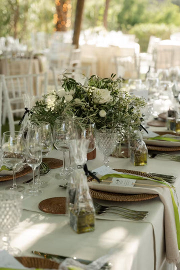 Mesa de banquete decorada con centro de flores blancas y ramas de olivo copas y cubiertos