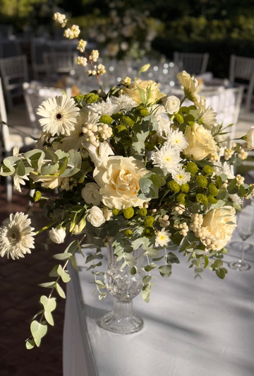 Arreglo floral con rosas blancas gerberas y follaje verde en un florero de cristal sobre una mesa