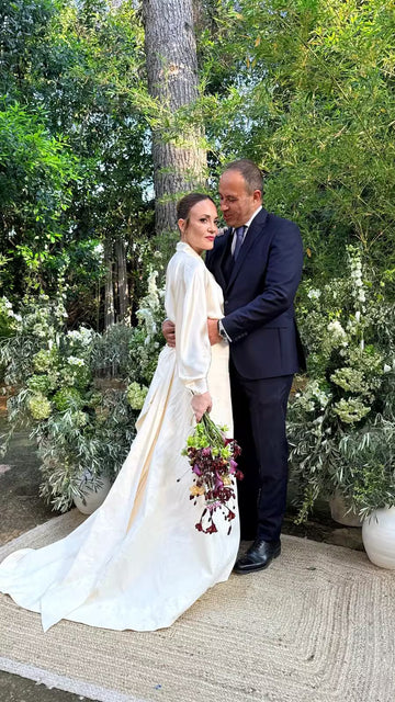 Novios vestidos de boda posando juntos en un jardín con arreglos florales