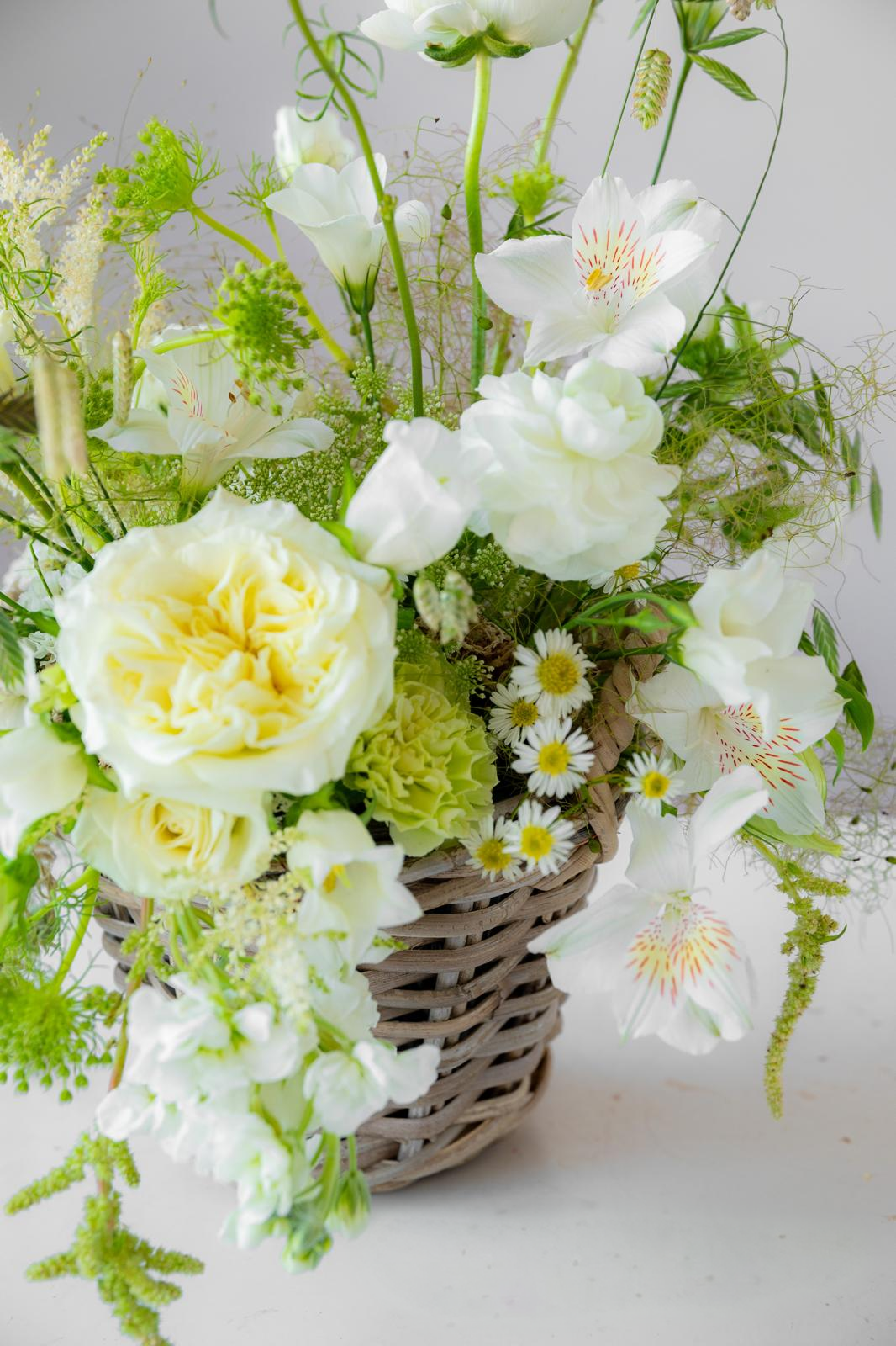 Arreglo floral blanco y verde con rosas, alstroemeria y margaritas en cesta de mimbre