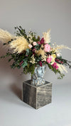 Arreglo floral con plumas de pampas y rosas en jarrón de rostro sobre pedestal de mármol