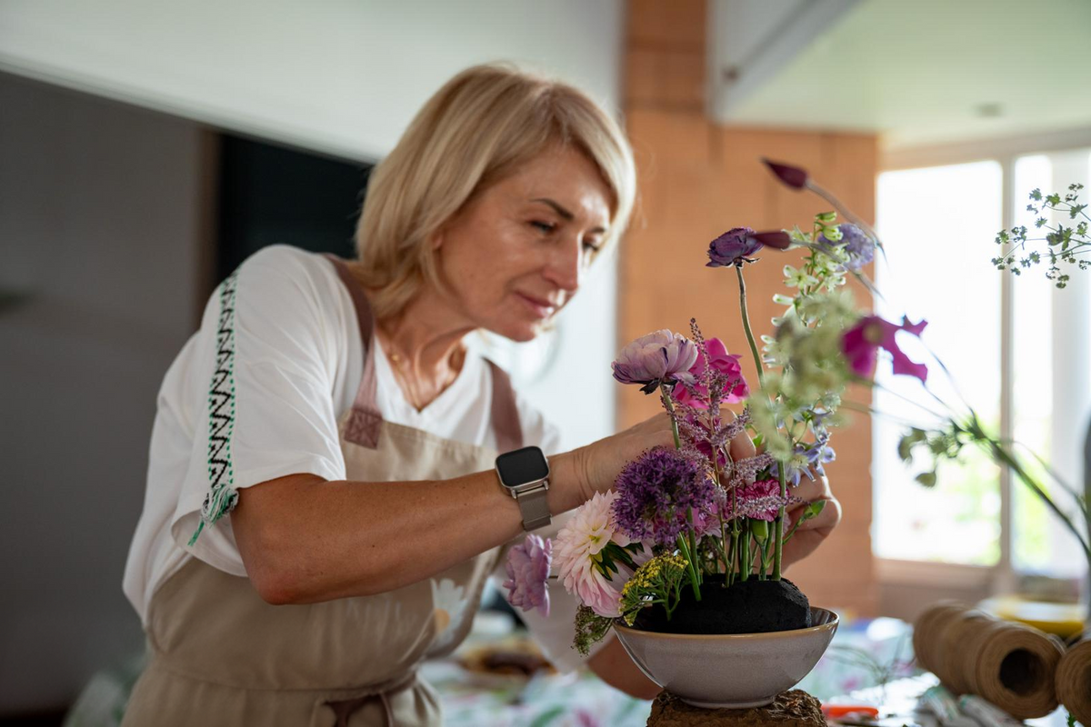 Mujer rubia con delantal creando un arreglo floral en un cuenco de cerámica