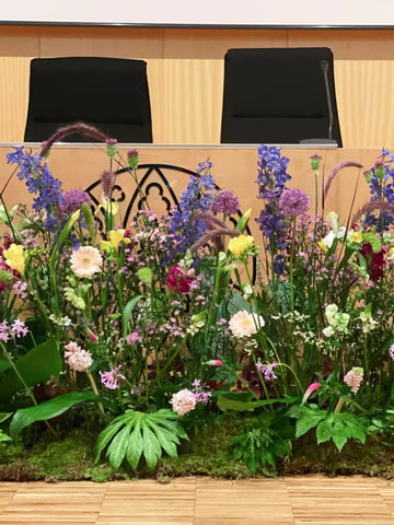 Arreglo floral variado con flores moradas amarillas y rosas sobre una mesa frente a sillas negras
