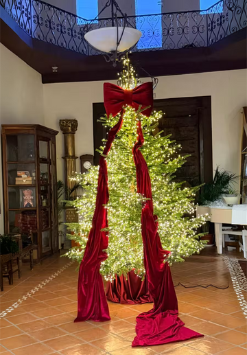 Arbol de Navidad iluminado con un gran lazo de terciopelo rojo en la parte superior