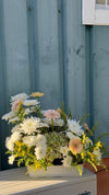 Centro floral de crisantemos blancos, gerberas rosa pastel, hortensia verde y solidago amarillo en jardinera blanca