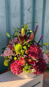 Centro floral con hortensias granates, lilium rosa, crisantemos verdes y lilas y liatris morado en maceta blanca