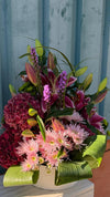 Centro floral con lilium, liatris morado, hortensia granate y crisantemos rosas rodeados de hojas verdes enrolladas