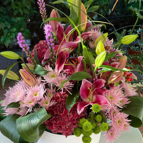 Centro floral con lilium rosa, crisantemos rosas y verdes, hortensia granate, liatris e hypericum en maceta blanca