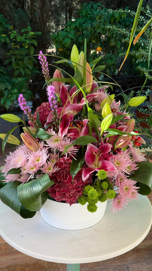 Centro floral con lilium rosa, crisantemos rosas y verdes, hortensia granate, liatris e hypericum en maceta blanca
