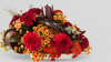 Centro de mesa bajo con crisantemos rojos, naranjas y amarillos, leucadendron y hojas trenzadas en bandeja blanca