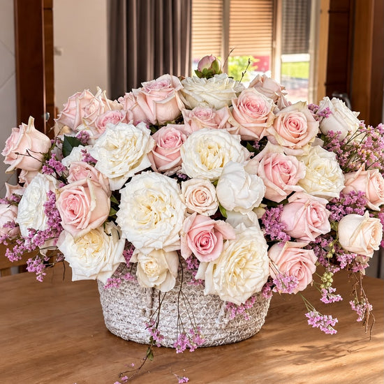 Centro de mesa con rosas blancas y rosas en cesta de mimbre sobre mesa de madera