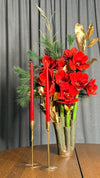 Centro navideño de amarilis rojas con pino y hojas doradas en jarrón de cerámica verde, junto a velas rojas, ANHUÁ Flowers Murcia