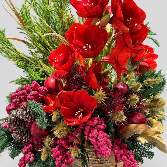 Centro navideño en cesta con amarilis rojas, protea, cardos dorados, piñas, bayas rosas y ramas de pino