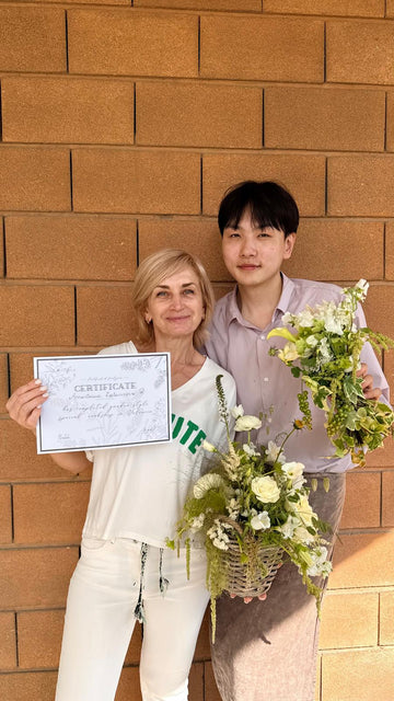 Mujer con certificado de floristería y hombre sosteniendo arreglo floral verde y blanco