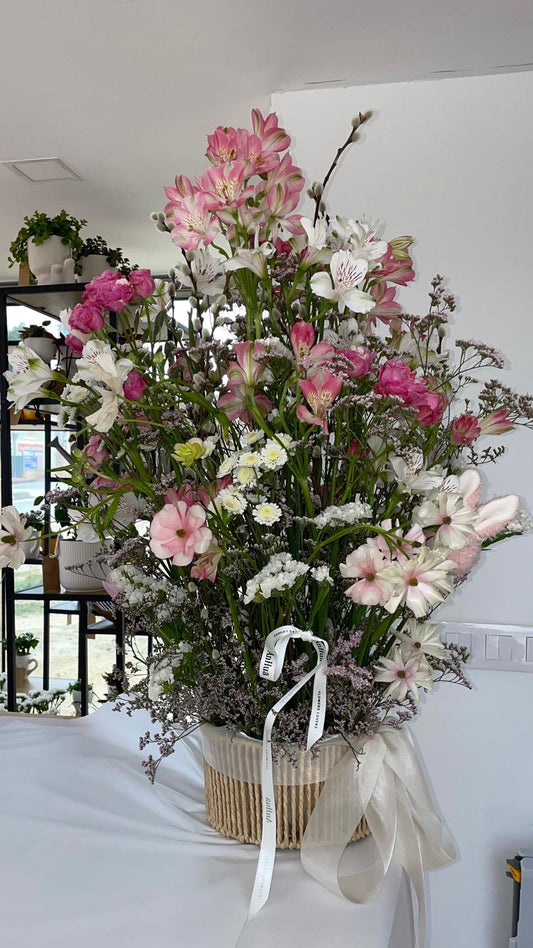 Cesta alta de flores con alstroemerias rosas y blancas, margaritas, limonium y ramas de sauce, con lazo blanco
