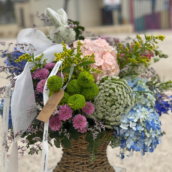 Cesta de mimbre con hortensias azules y rosas, crisantemos verdes y lilas, ammi, solidago y lazos de ANHUÁ Flowers