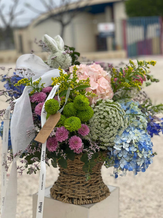 Cesta de mimbre con hortensias azules y rosas, crisantemos verdes y lilas, ammi, solidago y lazos de ANHUÁ Flowers