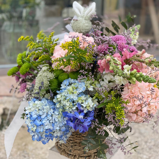 Cesta de flores con hortensias azules y rosas, bocas de dragón, delphinium, crisantemos y solidago