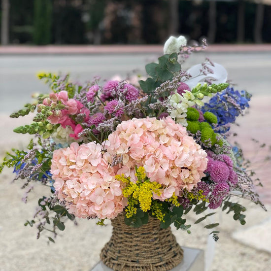 Cesta de flores con hortensias rosas, crisantemos morados, bocas de dragón, delphinium azul, solidago y eucalipto