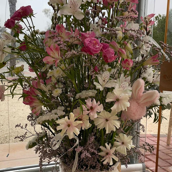 Cesta alta de flores rosas y blancas con alstroemerias, claveles y lazo de organza, en el escaparate de ANHUÁ Flowers