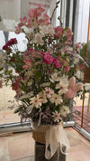 Cesta alta de flores rosas y blancas con alstroemerias, claveles y lazo de organza, en el escaparate de ANHUÁ Flowers