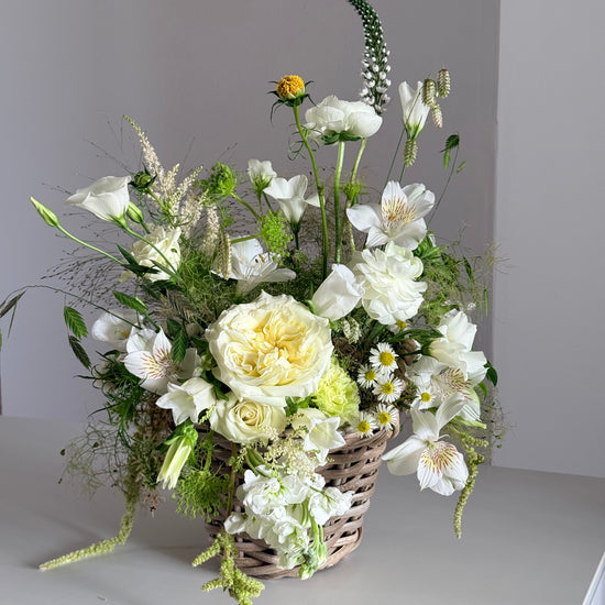 Cesta de mimbre con rosas blancas y alstroemeria sobre fondo neutro