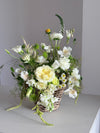 Cesta de mimbre con rosas blancas y alstroemeria sobre fondo neutro