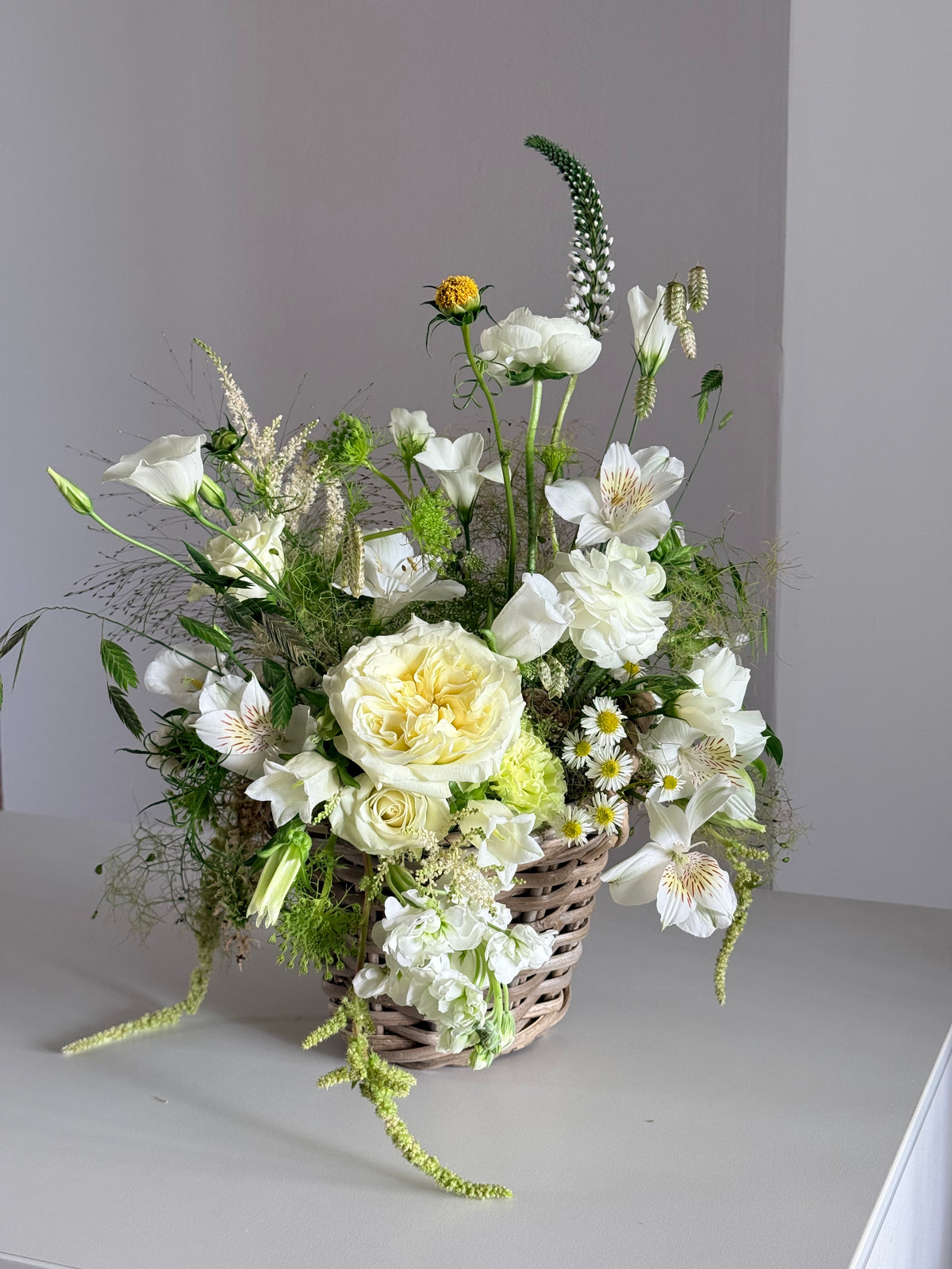 Cesta de mimbre con rosas blancas y alstroemeria sobre fondo neutro