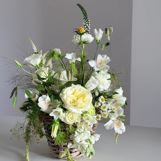 Cesta de mimbre con rosas blancas y alstroemeria, vista lateral sobre fondo gris