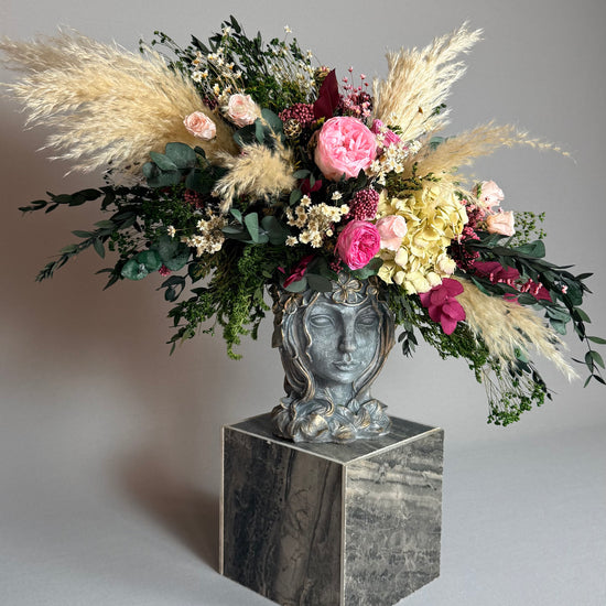 Composición floral completa en jarrón de rostro sobre pedestal de mármol