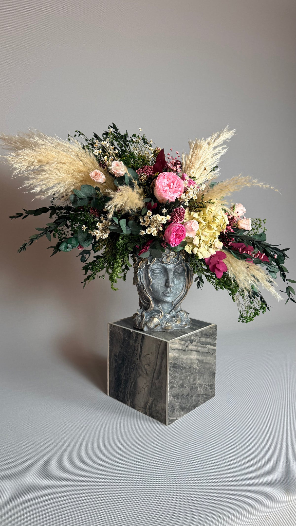 Composición floral completa en jarrón de rostro sobre pedestal de mármol