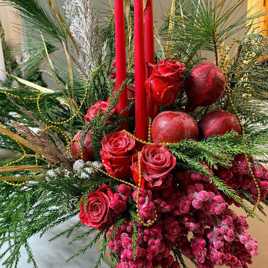Composición navideña con velas rojas, rosas rojas escarchadas, granadas, bayas rojas, ramas de pino y guirnalda dorada