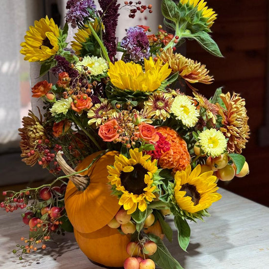 Composición otoñal en calabaza con girasoles, rosas naranjas, crisantemos, amaranto, bayas y manzanas ornamentales