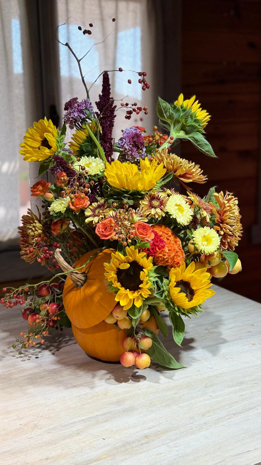Composición otoñal en calabaza con girasoles, rosas naranjas, crisantemos, amaranto, bayas y manzanas ornamentales
