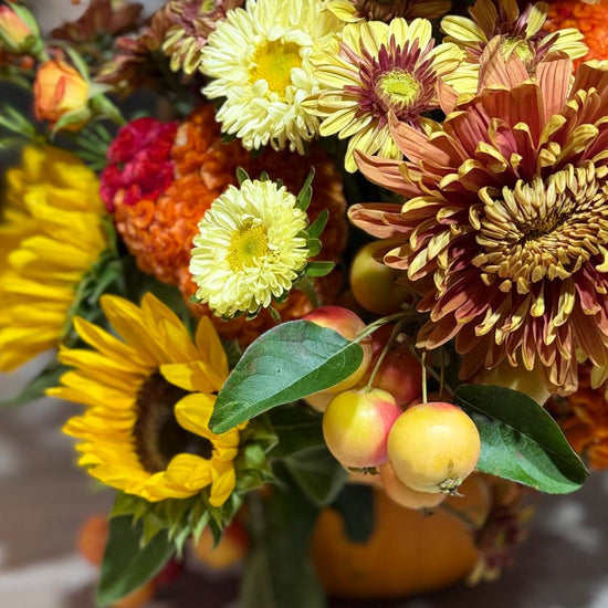 Detalle de composición otoñal con girasoles, crisantemos amarillos y cobrizos, celosía naranja y manzanas ornamentales