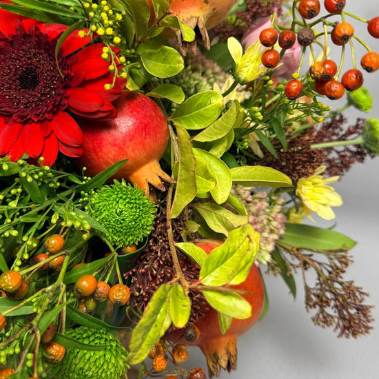 Detalle de composición otoñal con granadas, gerbera roja, lisianthus rosa, bayas naranjas y crisantemo verde