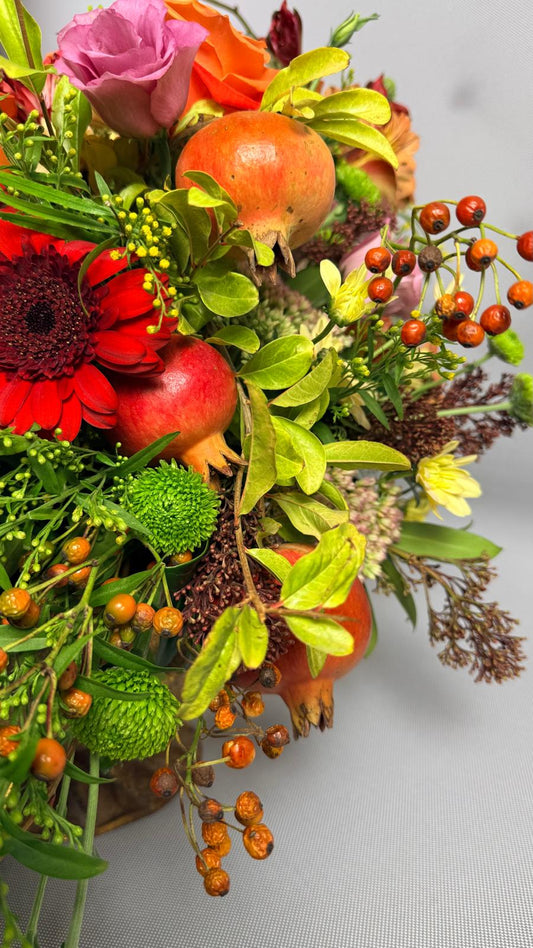 Detalle de composición otoñal con granadas, gerbera roja, lisianthus rosa, bayas naranjas y crisantemo verde