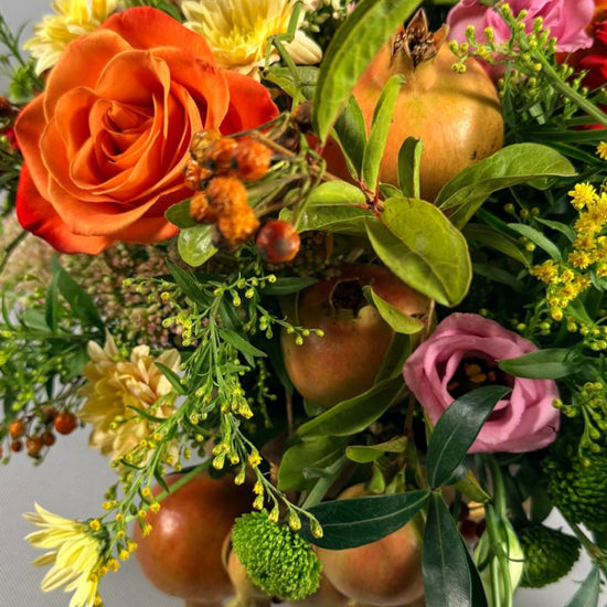 Detalle de composición otoñal con rosa naranja, lisianthus rosa, crisantemos amarillos, solidago y granadas