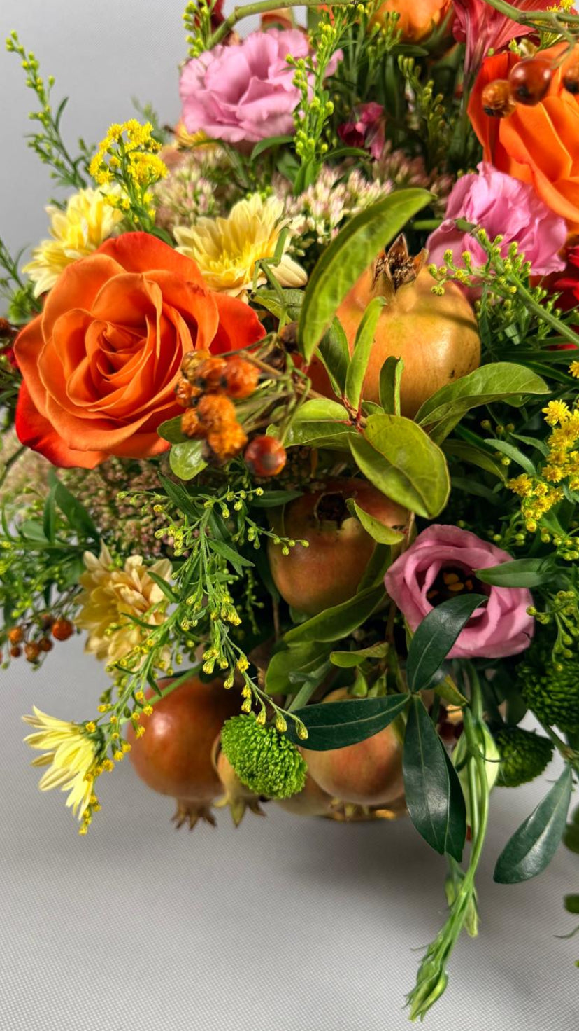 Detalle de composición otoñal con rosa naranja, lisianthus rosa, crisantemos amarillos, solidago y granadas