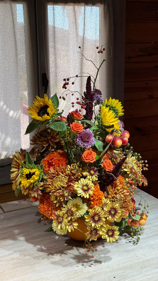 Composición otoñal con girasoles, rosas naranjas, crisantemos, celosía, amaranto, escabiosas y manzanas ornamentales junto a una ventana