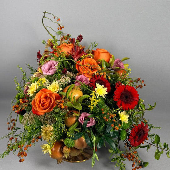 Composición floral otoñal con rosas naranjas, gerberas rojas, lisianthus rosa, crisantemos amarillos y granadas