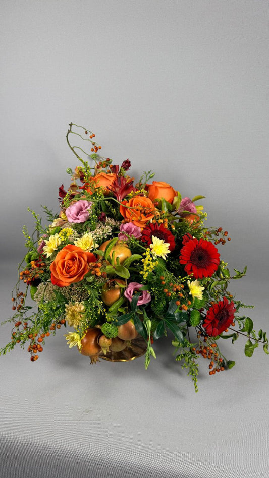Composición floral otoñal con rosas naranjas, gerberas rojas, lisianthus rosa, crisantemos amarillos y granadas