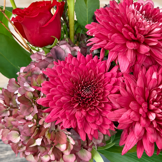 Composición floral con rosas rojas, crisantemos fucsia, hortensias rosa envejecidas y liatris en maceta gris