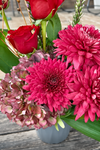 Composición floral con rosas rojas, crisantemos fucsia, hortensias rosa envejecidas y liatris en maceta gris
