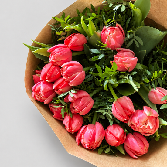Ramo de tulipanes dobles color coral con verdes frescos, envuelto en papel kraft