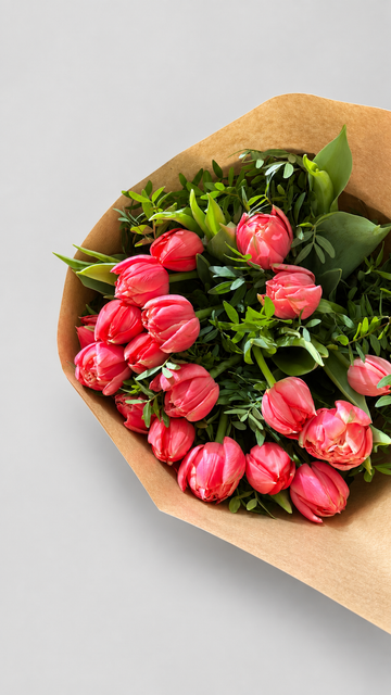 Ramo de tulipanes dobles color coral con verdes frescos, envuelto en papel kraft