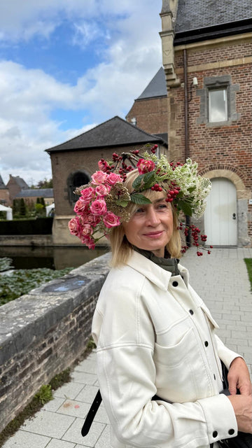 Mujer con corona floral de rosas rosas y bayas rojas frente a castillo