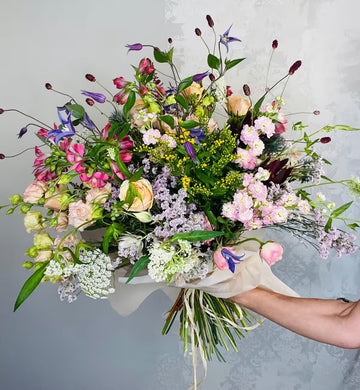 Ramo de flores variadas con rosas, clemátides y flores silvestres envuelto en papel