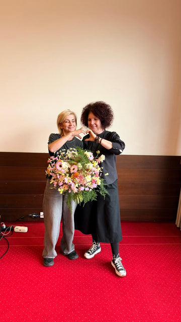 Dos mujeres sosteniendo un ramo de flores y formando un corazón con las manos